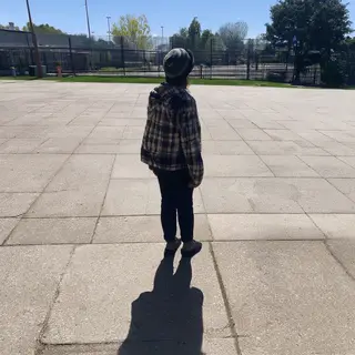 A person standing outdoors at midday with a short shadow dir