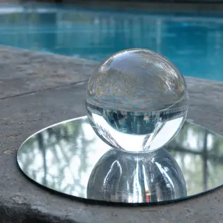 A clear glass sphere sitting on a mirror surface near a pool