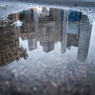 A city skyline reflected in a rain puddle on a street, with 