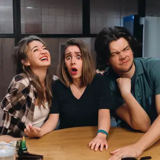 A group of three friends at a table: one laughing with head 