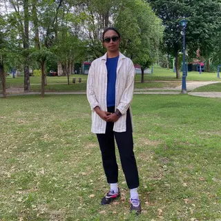 A person standing in a neutral pose in a park, full body vis