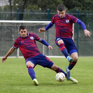 Two soccer players mid-tackle, one sliding and the other jum