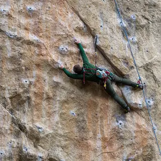 A rock climber clinging to a cliff face with arms and legs e