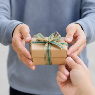 One person handing a small gift box to another person, both 