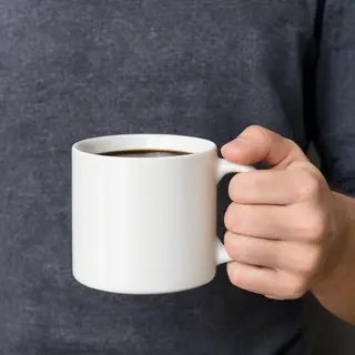 A person holding a white ceramic coffee mug by the handle wi