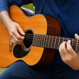 A person playing an acoustic guitar with left hand on the fr