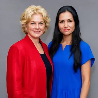 Two women standing side by side: one with short blonde hair 