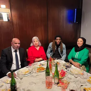 Four people at a dinner table: a bald man in a suit, a woman