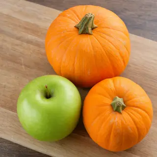 A green apple and an orange pumpkin on a wooden cutting boar