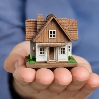 A miniature house sitting on the palm of someone's hand