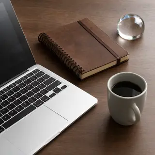 A workspace desk with a brushed aluminum laptop, a leather-b