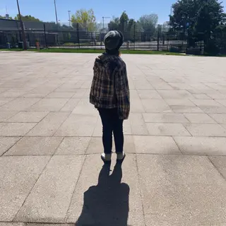 A person standing outdoors at midday with a short shadow dir