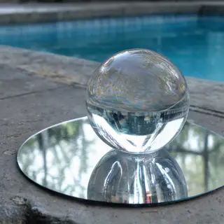 A clear glass sphere sitting on a mirror surface near a pool
