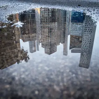 A city skyline reflected in a rain puddle on a street, with 