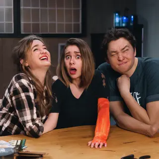 A group of three friends at a table: one laughing with head 