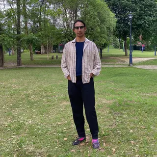 A person standing in a neutral pose in a park, full body vis