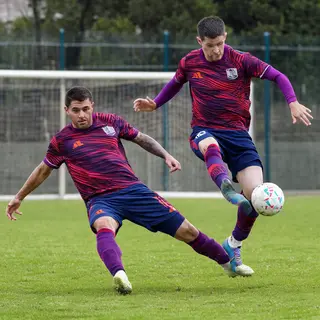 Two soccer players mid-tackle, one sliding and the other jum