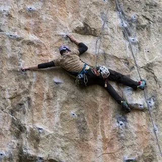 A rock climber clinging to a cliff face with arms and legs e