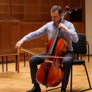 A cellist seated with correct posture, legs around the instr