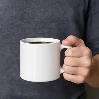 A person holding a white ceramic coffee mug by the handle wi