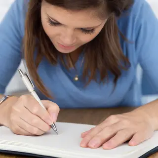 A woman writing in a notebook with a pen gripped correctly i