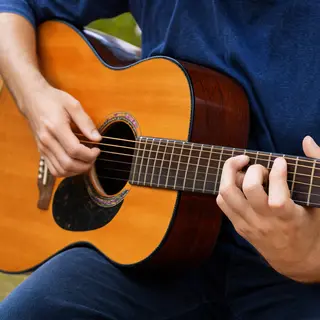 A person playing an acoustic guitar with left hand on the fr