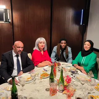 Four people at a dinner table: a bald man in a suit, a woman
