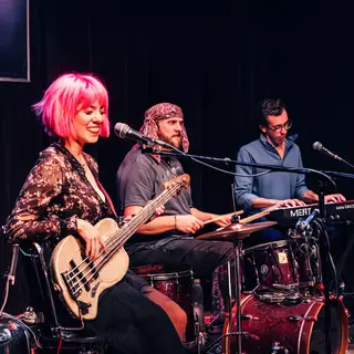 Three musicians on stage: a tall woman with short pink hair 