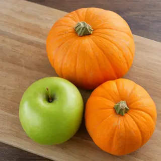 A green apple and an orange pumpkin on a wooden cutting boar