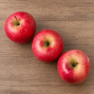 Exactly 3 red apples arranged on a wooden table
