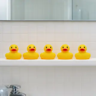 Exactly 5 yellow rubber ducks sitting in a row on a bathroom
