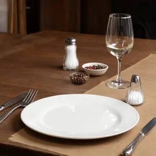 A dinner table scene with a plate, fork, knife, wine glass, 