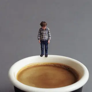 A tiny person standing on the rim of a coffee cup, looking d