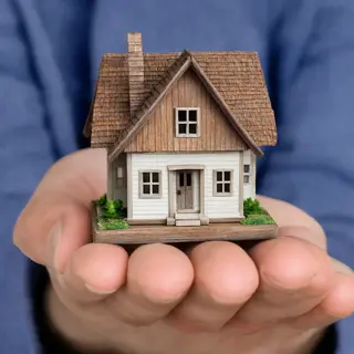 A miniature house sitting on the palm of someone's hand
