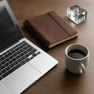 A workspace desk with a brushed aluminum laptop, a leather-b