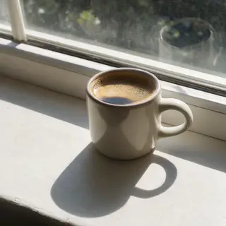 A coffee mug on a sunny windowsill casting a sharp shadow to