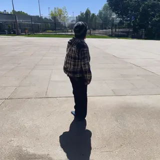 A person standing outdoors at midday with a short shadow dir