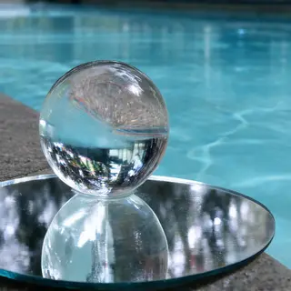 A clear glass sphere sitting on a mirror surface near a pool