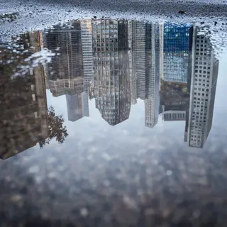 A city skyline reflected in a rain puddle on a street, with 