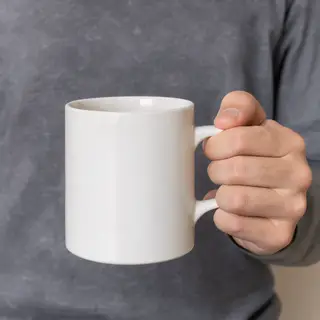A person holding a white ceramic coffee mug by the handle wi