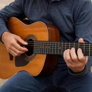 A person playing an acoustic guitar with left hand on the fr