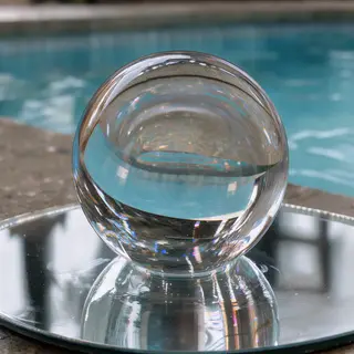 A clear glass sphere sitting on a mirror surface near a pool