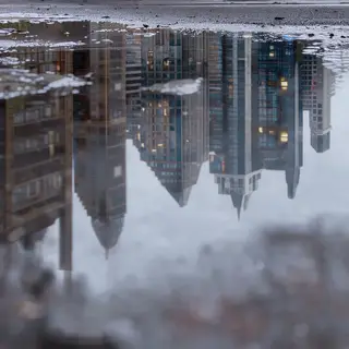 A city skyline reflected in a rain puddle on a street, with 