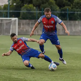 Two soccer players mid-tackle, one sliding and the other jum