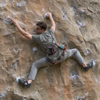 A rock climber clinging to a cliff face with arms and legs e