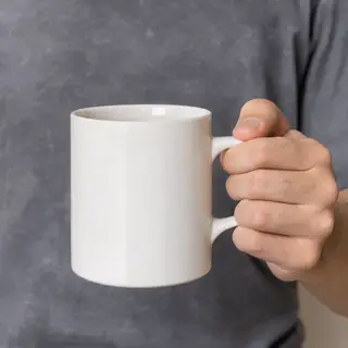 A person holding a white ceramic coffee mug by the handle wi