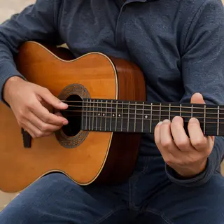 A person playing an acoustic guitar with left hand on the fr