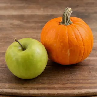 A green apple and an orange pumpkin on a wooden cutting boar