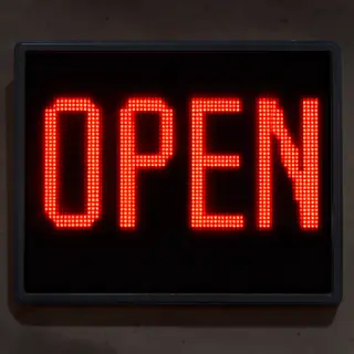 The word 'OPEN' displayed on a red LED sign with glowing pix