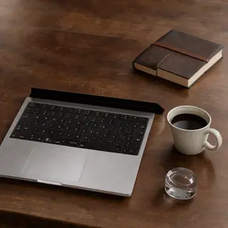 A workspace desk with a brushed aluminum laptop, a leather-b